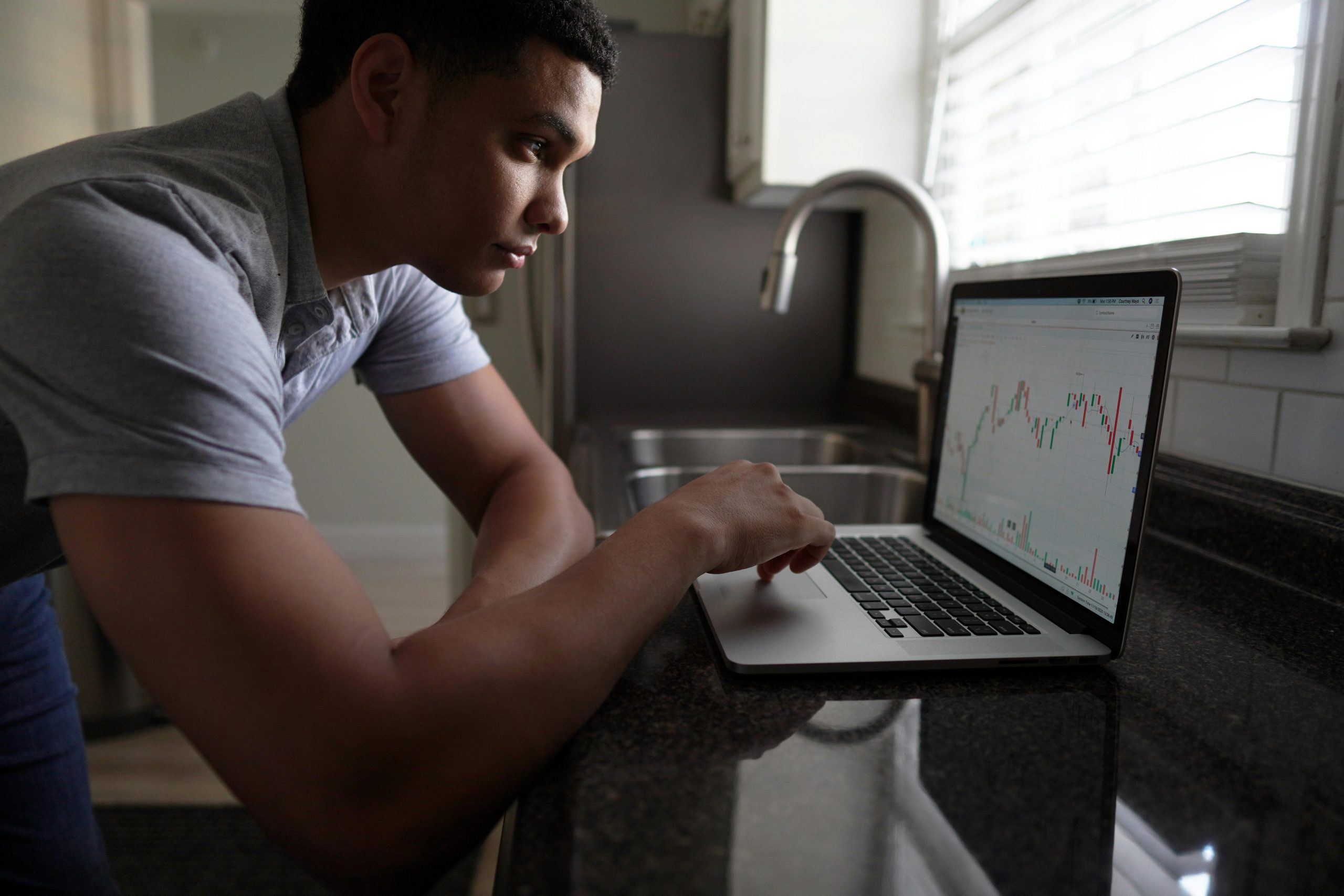 Focused man analyzing market trends on a laptop in a modern kitchen setting.