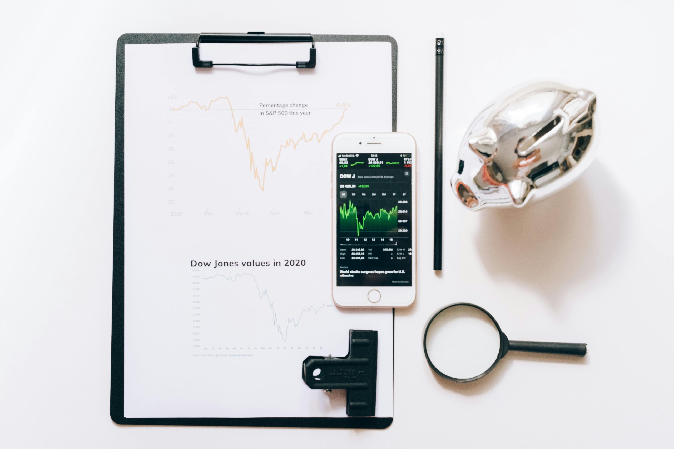 So Sánh Top 5 Công Ty Chứng Khoán Việt Nam 2026 Top view of financial analysis tools including a cellphone, clipboard, magnifying glass, and piggy bank on a white desk.