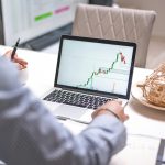 Top 5 Sàn Chứng Khoán Uy Tín Việt Nam 2026 Phí Thấp Person analyzing stock market trends on laptop in a modern home office setting.